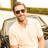 Man wearing Polygon Aviator sunglasses with brown polarized lenses, leaning on a car