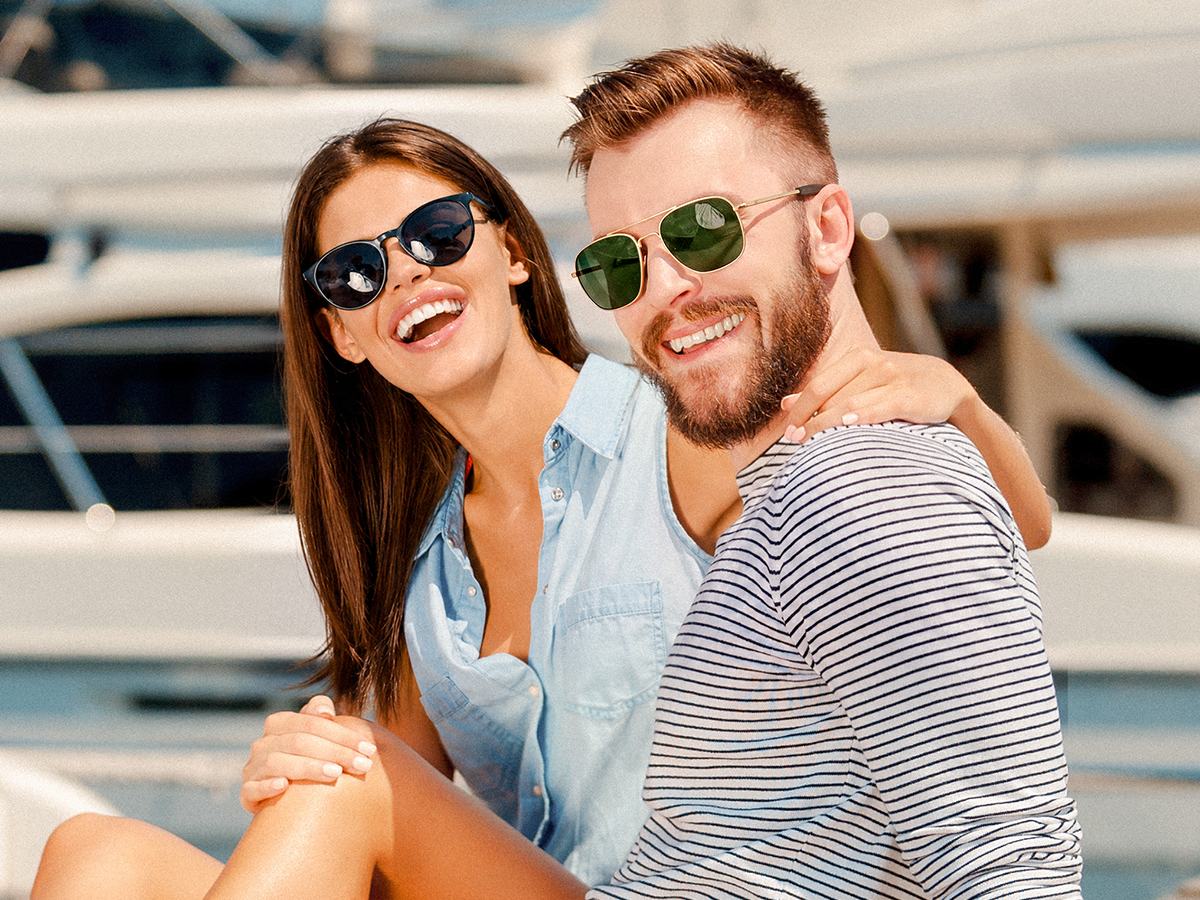 Smiling couple wearing sunglasses by the water at a marina